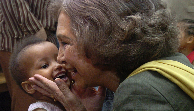 Un niño pequeño sonrie acompañado de S.M. la Reina Doña Sofía en un evento de la Fundación